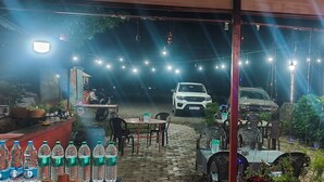 Un espacio al aire libre con mesas, sillas, un automóvil y luces colgantes.