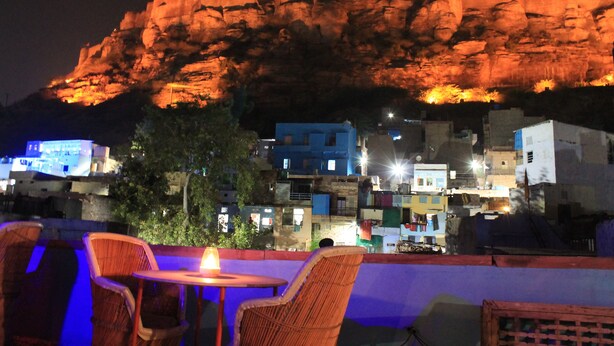 A night view of a town with a prominent rock formation illuminated in the background. - Kesar Heritage Guest House  (Jodhpur)