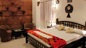 A bedroom with a large bed, two chairs, a small table, a nightstand, a wall-mounted clock, and a curtain. - Kesar Heritage Guest House  (Jodhpur)