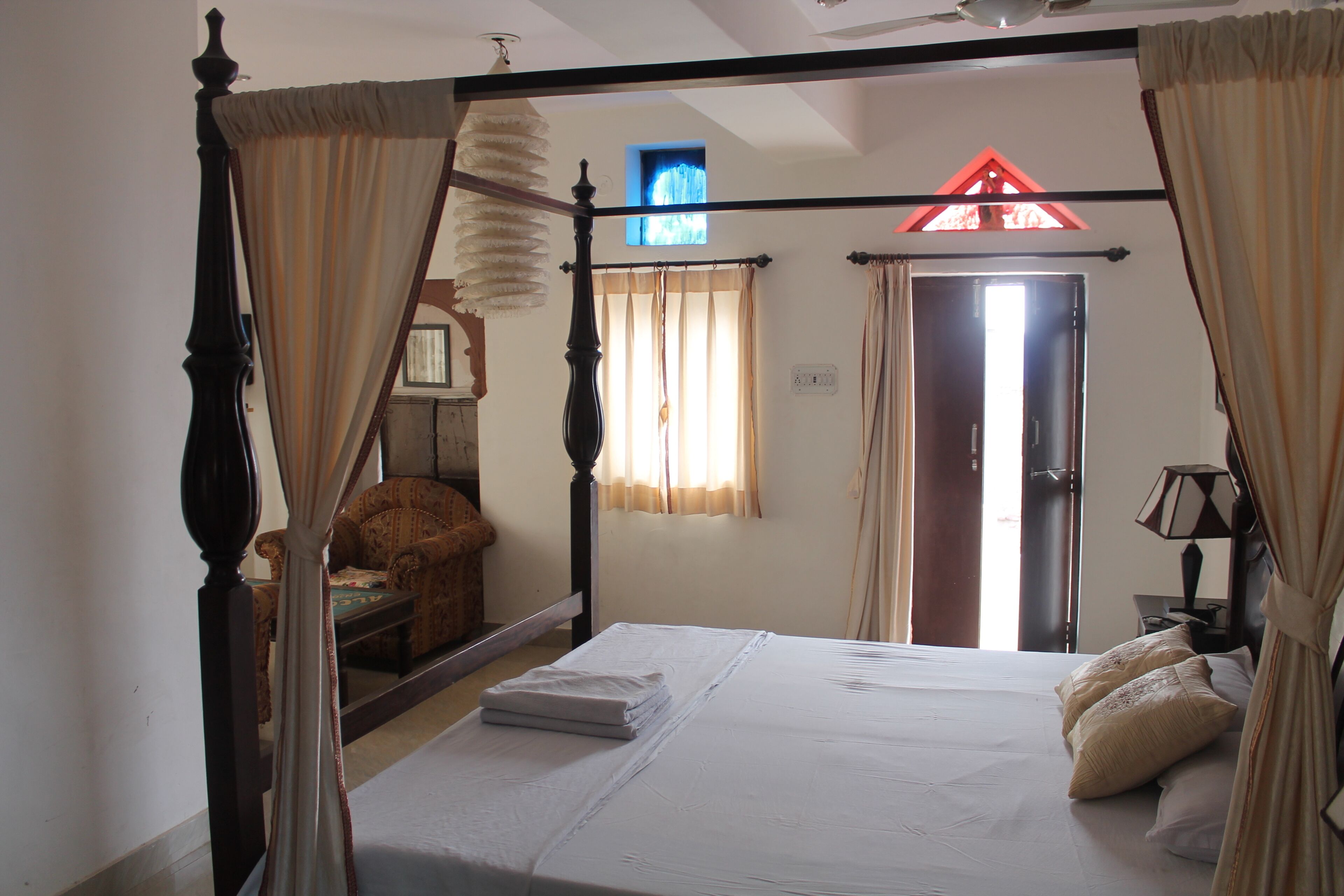 A four-poster bed with curtains, a chair, a lamp, and a window with curtains.