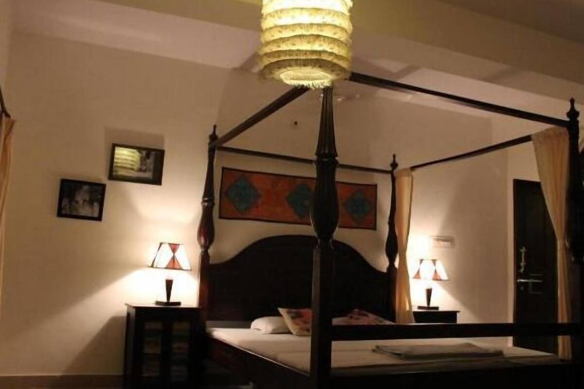 A four-poster bed with a canopy, two bedside lamps, and a framed artwork on the wall.