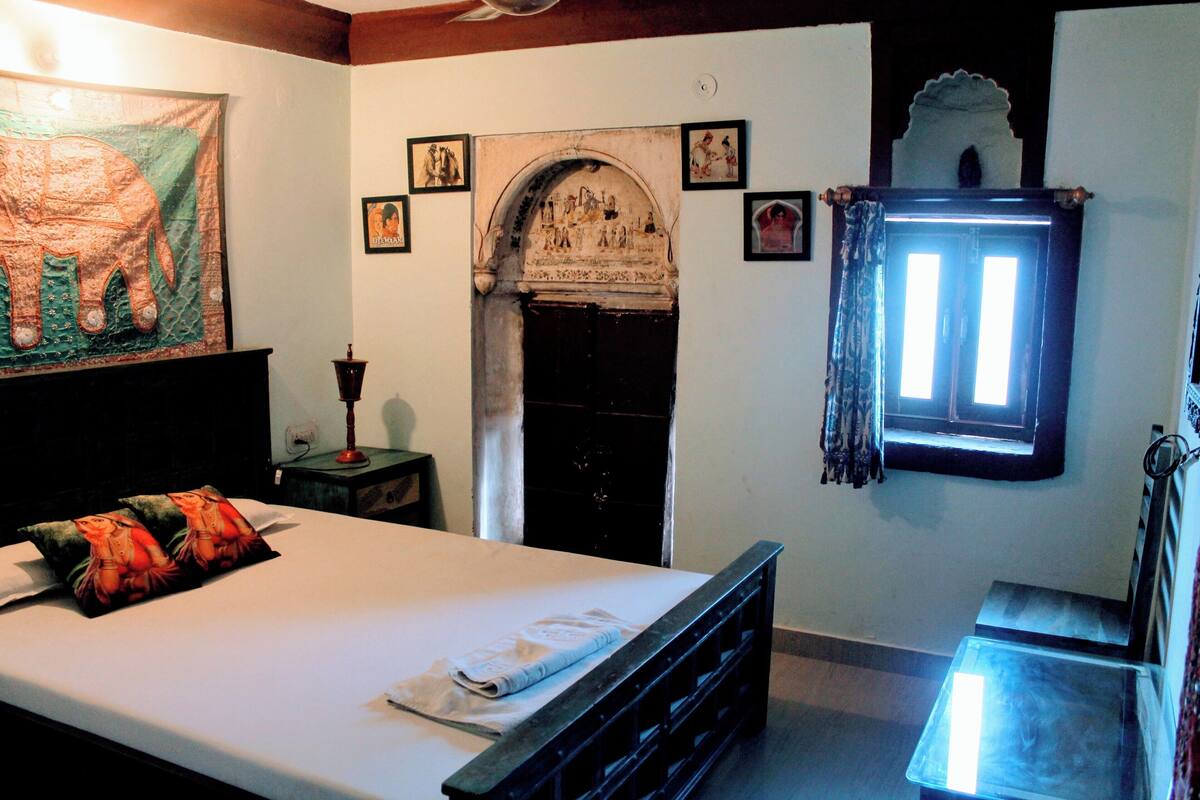 A room with a bed, a fireplace, a window with curtains, and a tapestry on the wall.