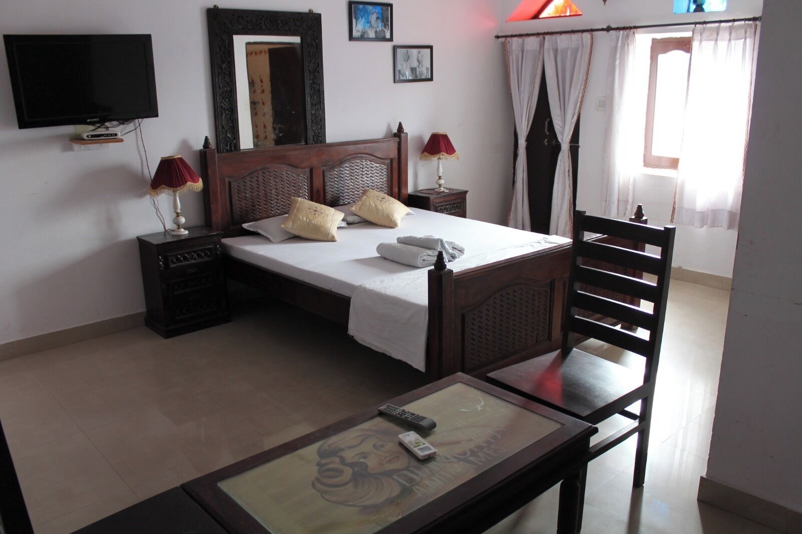 A bedroom with a bed, bedside tables, a TV, a chair, and a table with a remote control.