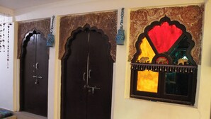 A room with two dark wooden doors, a small window with decorative elements, and a wall-mounted light fixture. - Kesar Heritage Guest House  (Jodhpur)