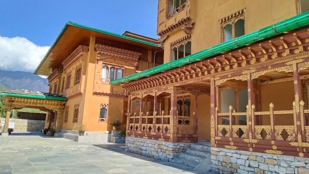 Un edificio tradicional con un patio de piedra, balcones de madera ornamentados y techo verde.