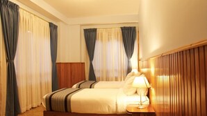 Una habitación de hotel con dos camas, cabecero de madera, lámpara de noche y cortinas.