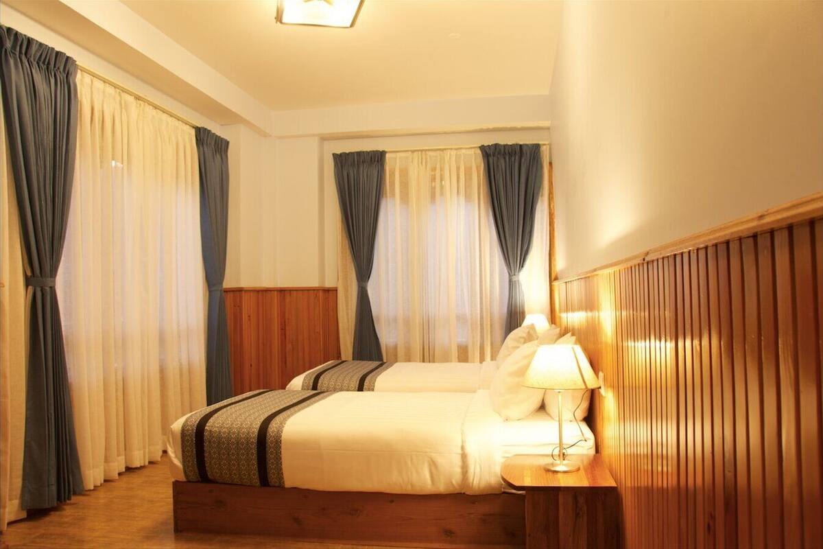 A hotel room with two beds, a wooden headboard, a bedside lamp, and curtains.