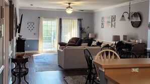 A spacious living area with a sofa, dining table, and chairs, a kitchen area with a counter and cabinets, and a hallway leading to a door. - The retreat at Magnolia (Myrtle Beach)