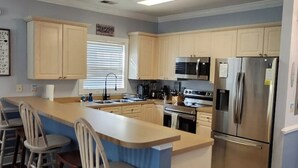 A modern kitchen with a central island, bar stools, stainless steel appliances, and light-colored cabinetry. - The retreat at Magnolia (Myrtle Beach)