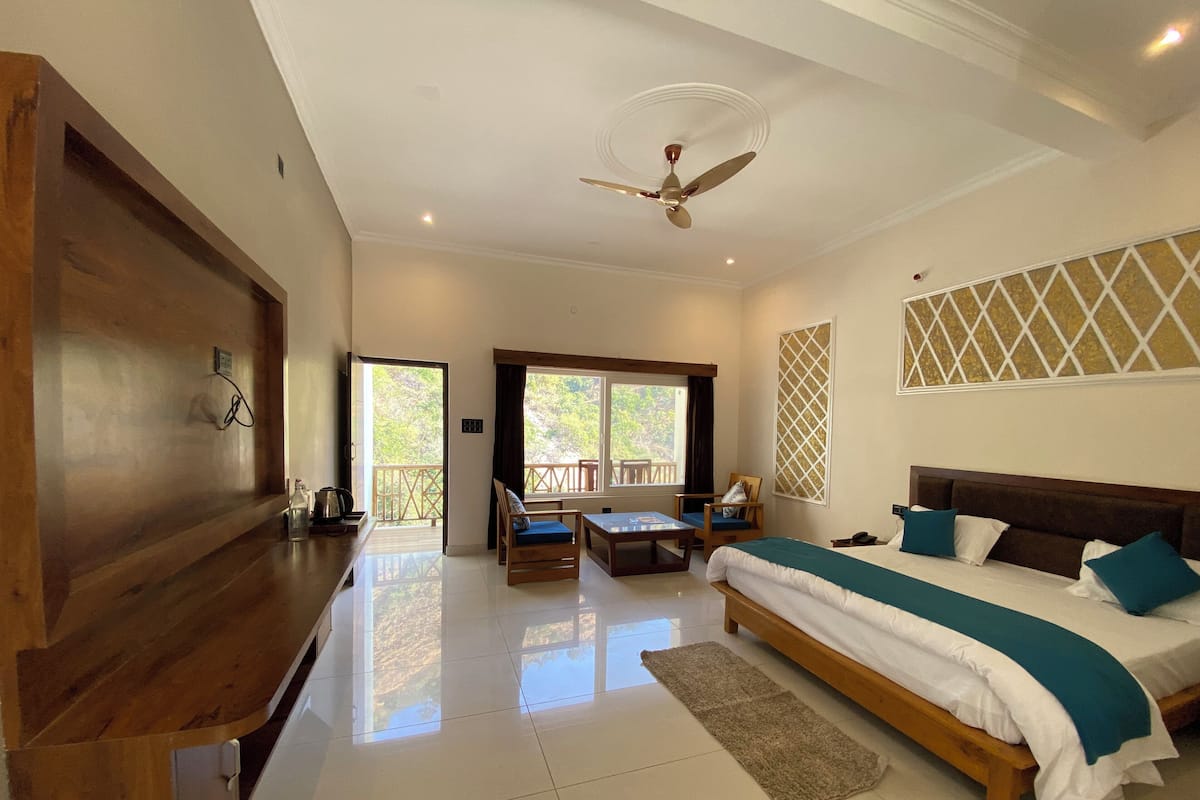 A bedroom with a bed, a desk, a chair, and a balcony with a view of greenery.