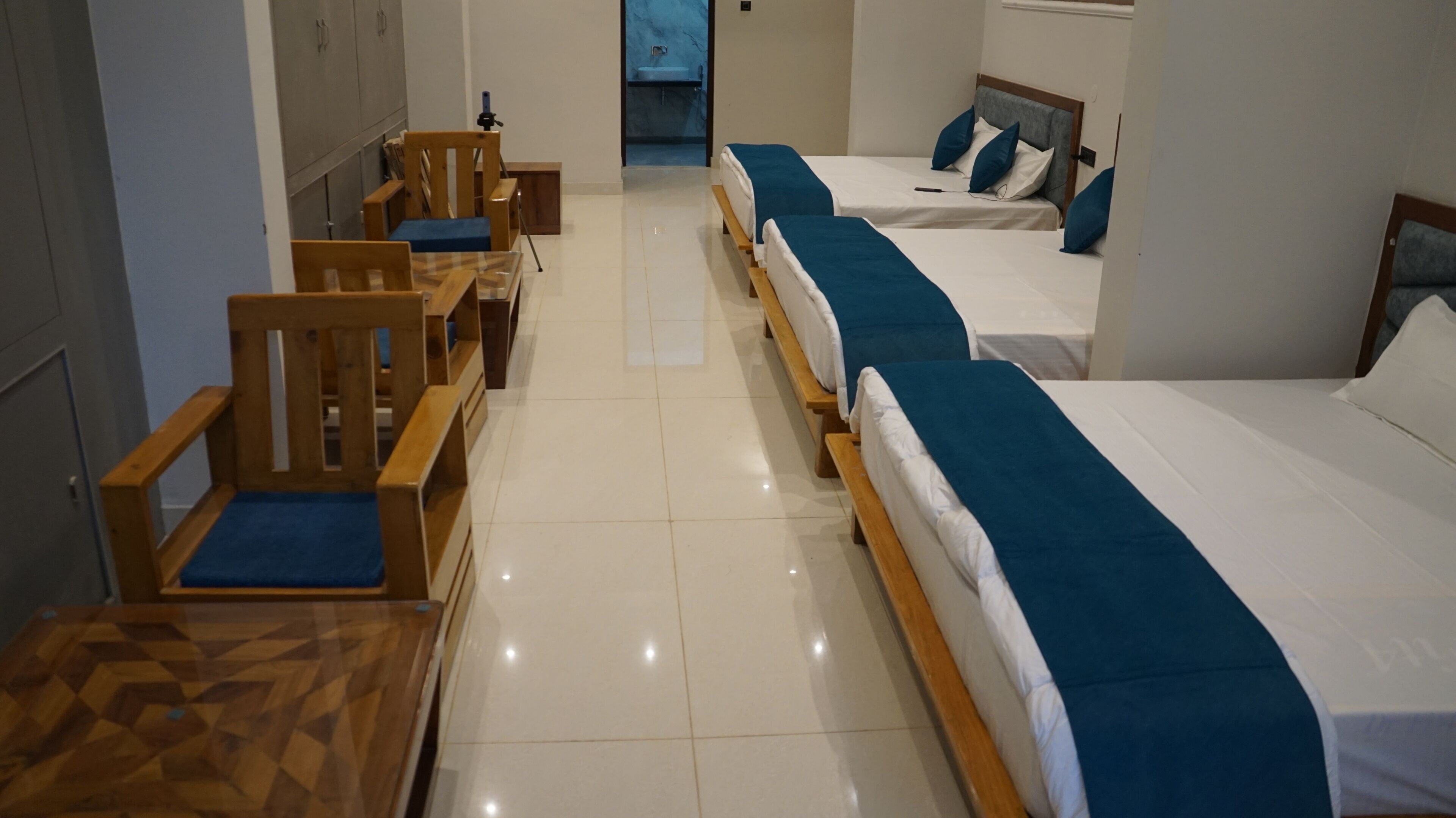Habitación de hotel con dos camas individuales, una silla de madera, una mesita y un baño visible a través de una puerta abierta.