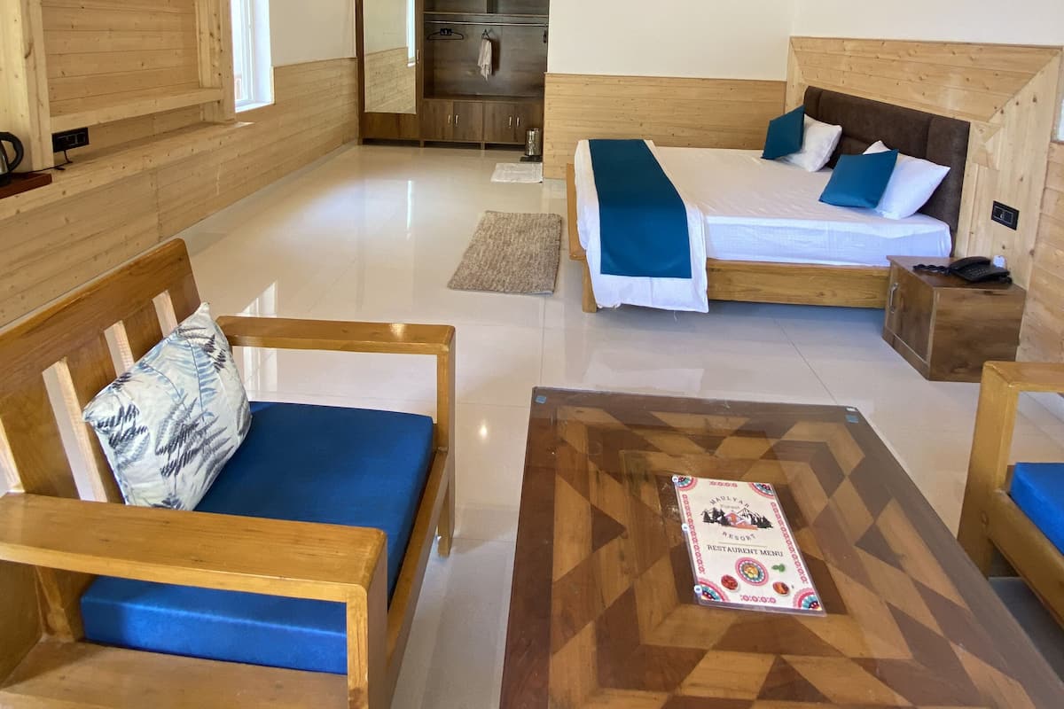 A modern hotel room with wooden walls and ceiling, a large bed with blue and white bedding, a wooden coffee table with a menu, and a seating area with blue cushioned chairs.