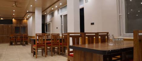 A spacious dining area with wooden tables and chairs, a large window, and a ceiling with recessed lighting.