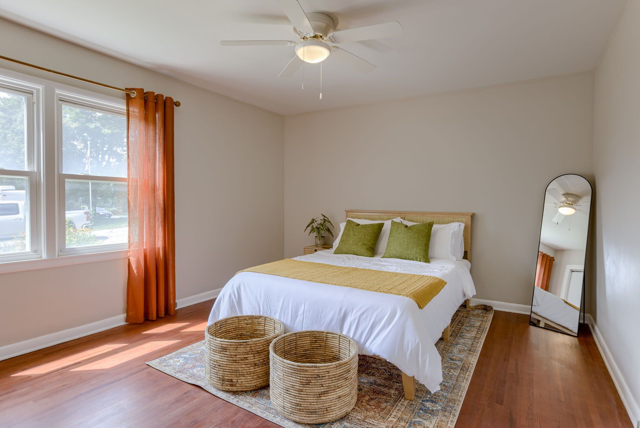 A bedroom with a bed, a ceiling fan, a large mirror, and a window with curtains.