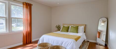 A bedroom with a bed, a ceiling fan, a large mirror, and a window with curtains.