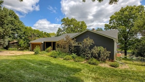 A single-story house with a covered porch, surrounded by a well-maintained lawn and trees. - 5BD Charming Home - Pool Table & Backyard (Omaha)