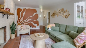 A living room with a green sofa, a round coffee table, a fireplace, and a wall with woven wall art. - 5BD Charming Home - Pool Table & Backyard (Omaha)