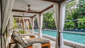 Un espace aménagé au bord de la piscine, avec des chaises longues et une vue sur une piscine entourée de verdure.