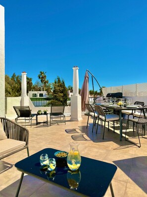 Een terras buiten met een eettafel, stoelen, een barbecue en een pergola.