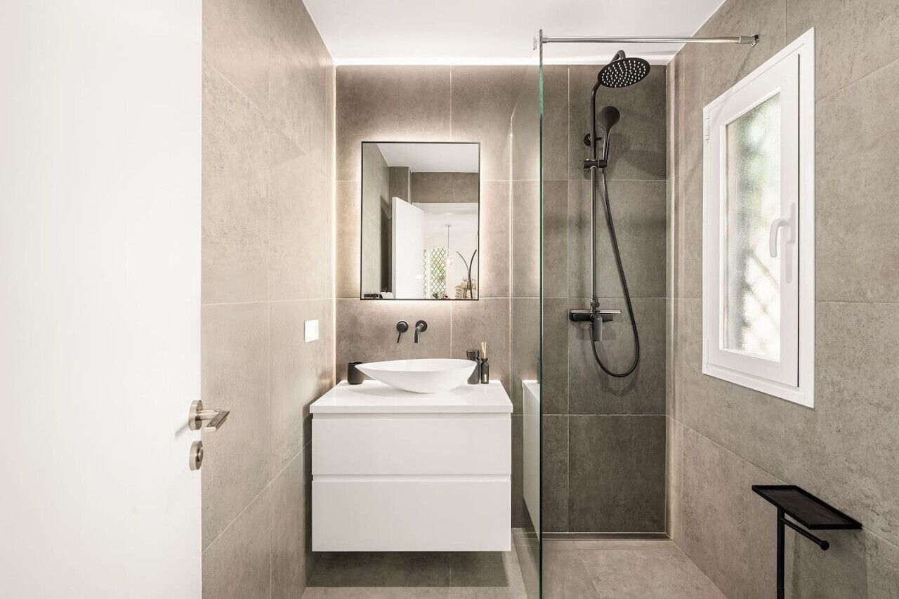 A modern bathroom with a large mirror, a white sink, and a glass-enclosed shower area.