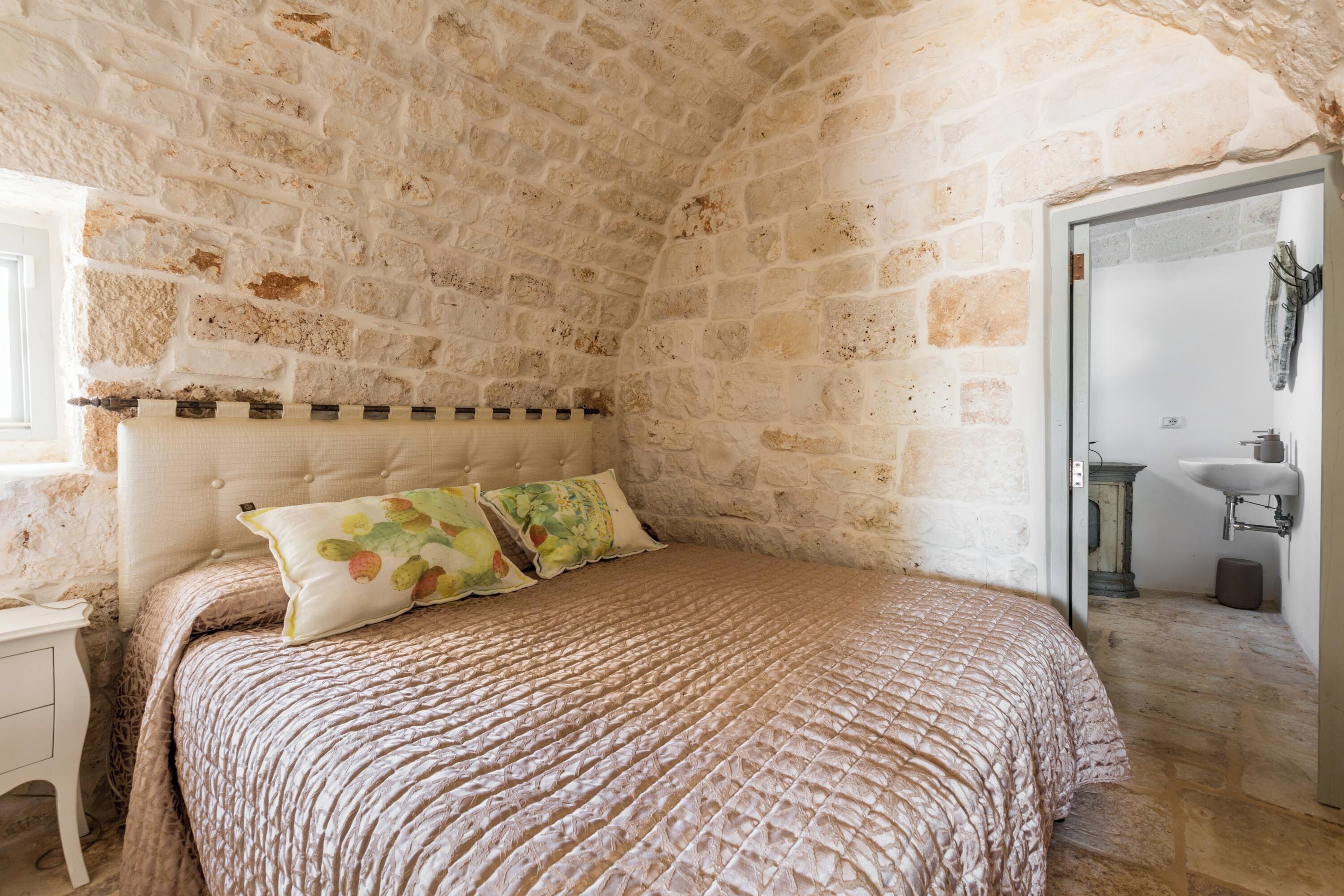 A bedroom with a stone wall, a bed with a patterned bedspread, and a nightstand.