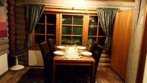 Un comedor con una mesa de madera dispuesta para cuatro personas, flanqueada por dos ventanas con cortinas.