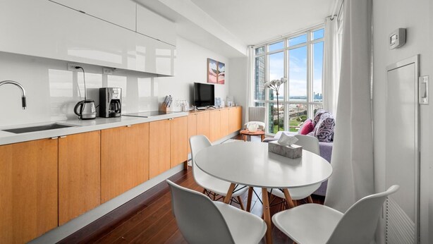 A modern kitchen with a large window, wooden cabinets, and a dining area with a round table and chairs. - GLOBALSTAY. Panoramic 1 Bedroom Condo in Downtown (Toronto/Canada)