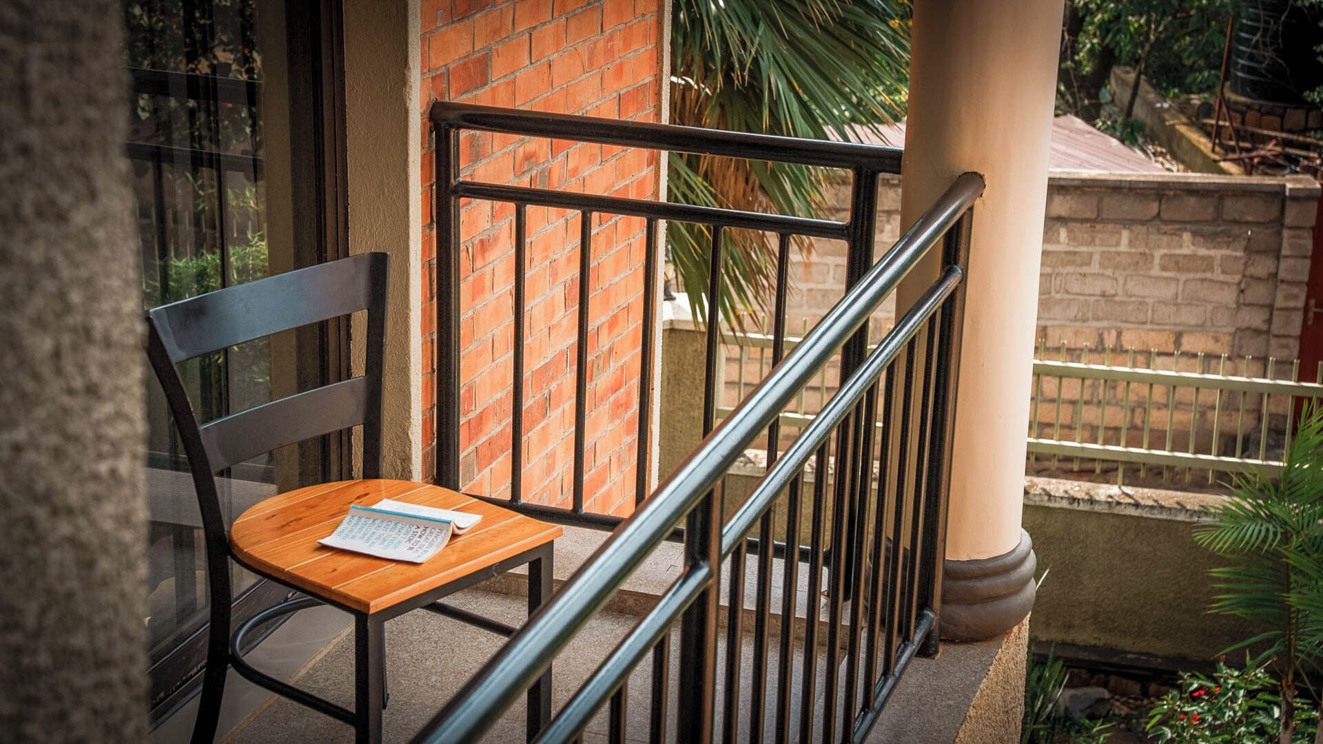 A wooden chair with a metal frame on a balcony with a brick wall and metal railing.