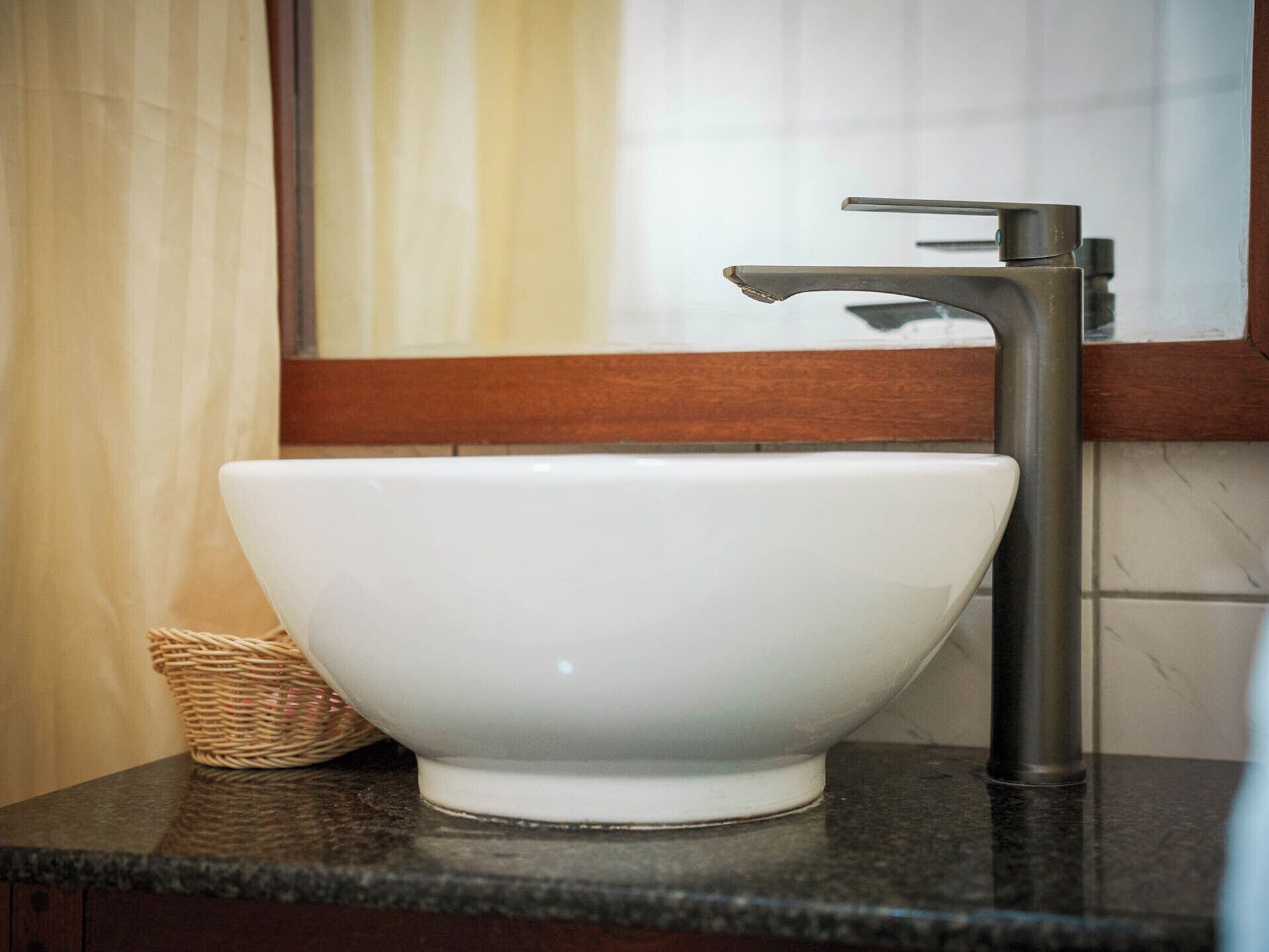 A white ceramic sink with a modern faucet on a dark countertop, set against a wooden panel and a tiled wall.