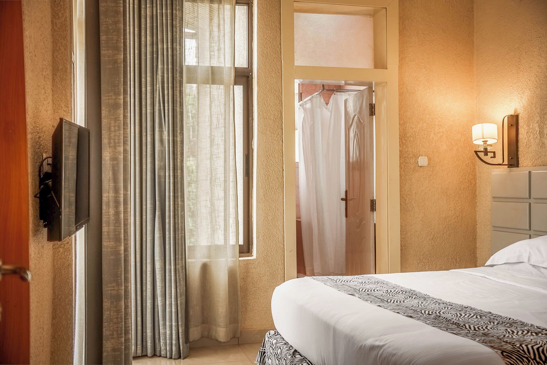 Hotelkamer met een bed, een aan de muur bevestigde televisie, een douchegedeelte en een badkamer met een handdoekhouder.