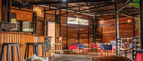 Interior rústico de restaurante con paredes de madera, barra y mesas dispuestas para comer.