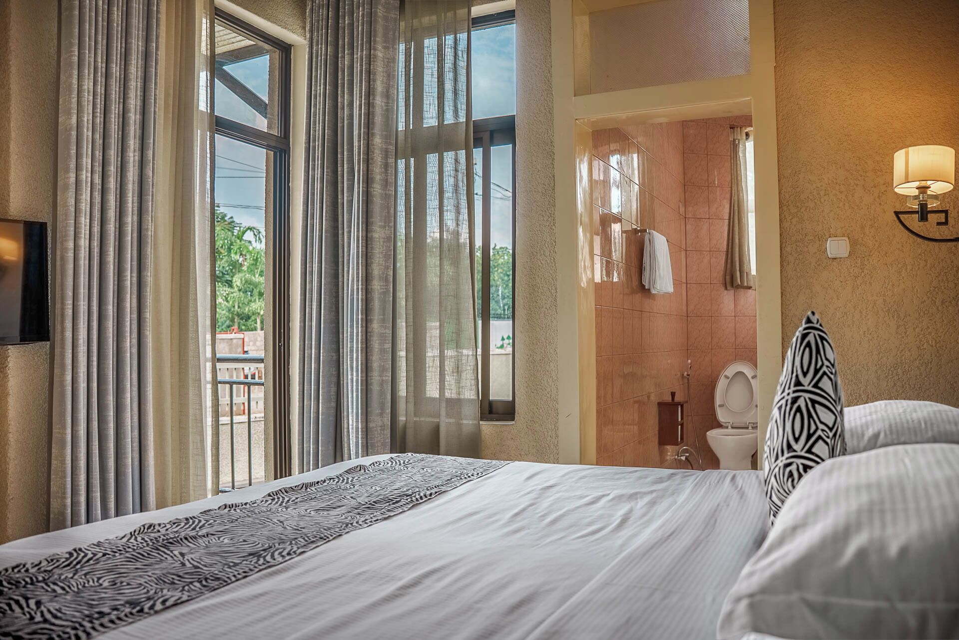 Habitación de hotel con una cama grande, un baño con inodoro y lavamanos, y vistas al exterior.