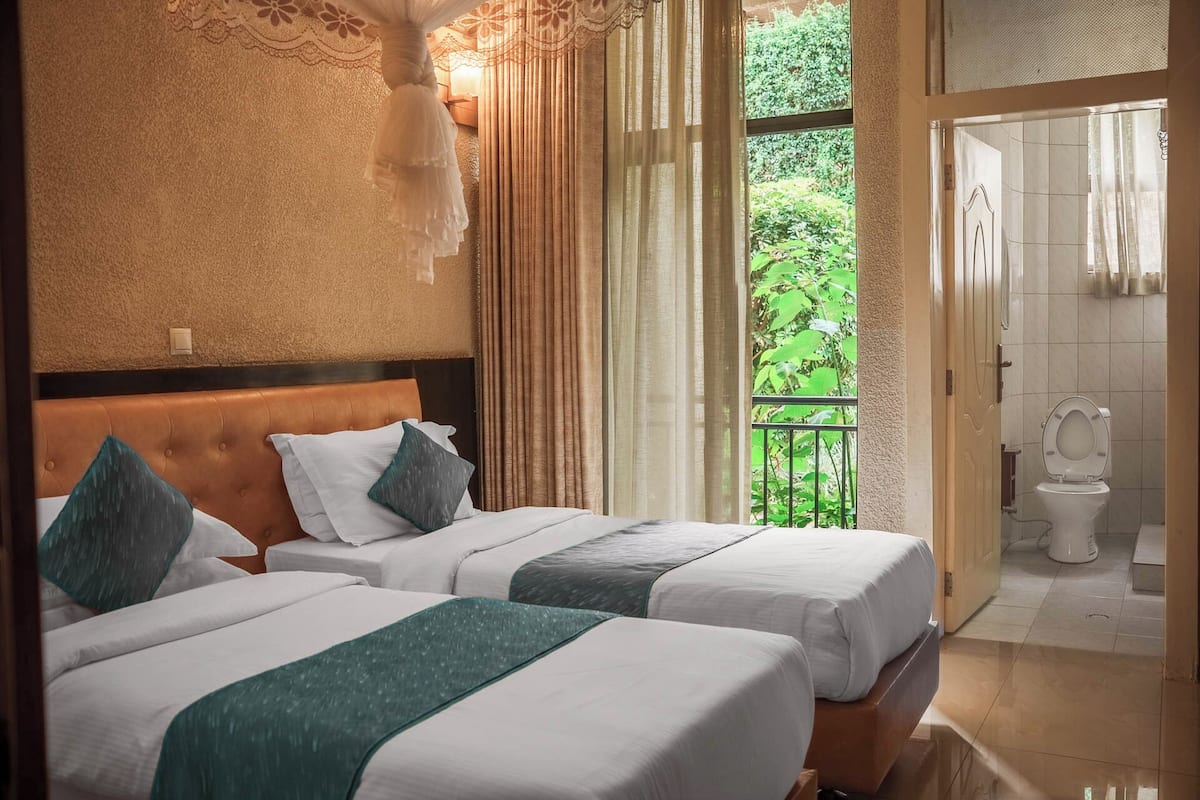Habitación de hotel con dos camas, un balcón con vistas a zonas verdes y un baño con inodoro y lavamanos.