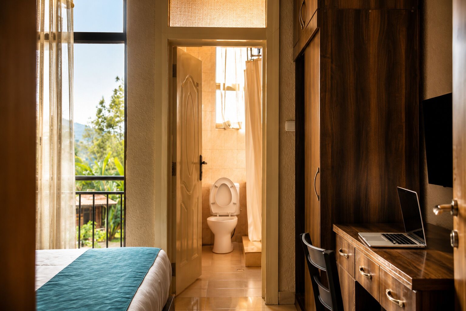 Et hotelværelse med en seng, et træskrivebord med en bærbar computer, et toilet og et bruseområde.