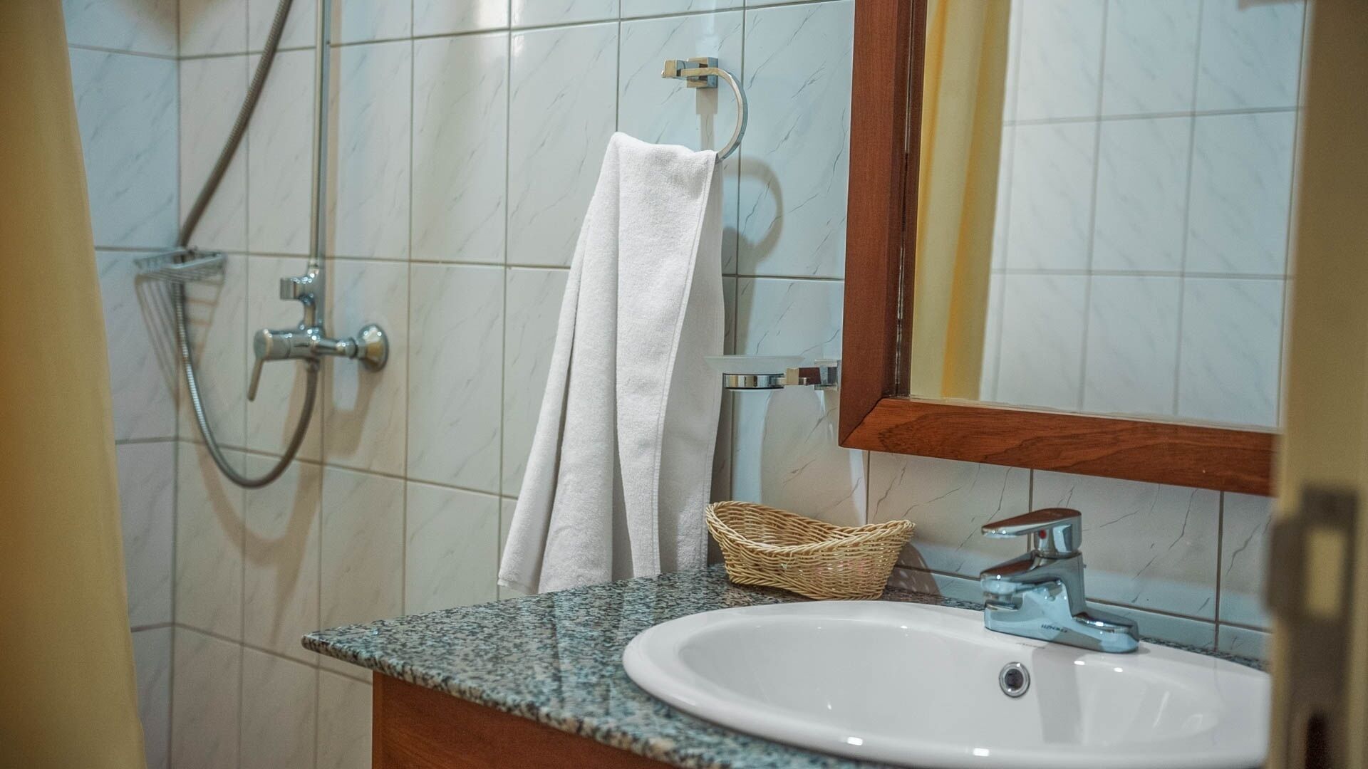 Un baño con lavamanos blanco, un espejo, toallero y ducha.