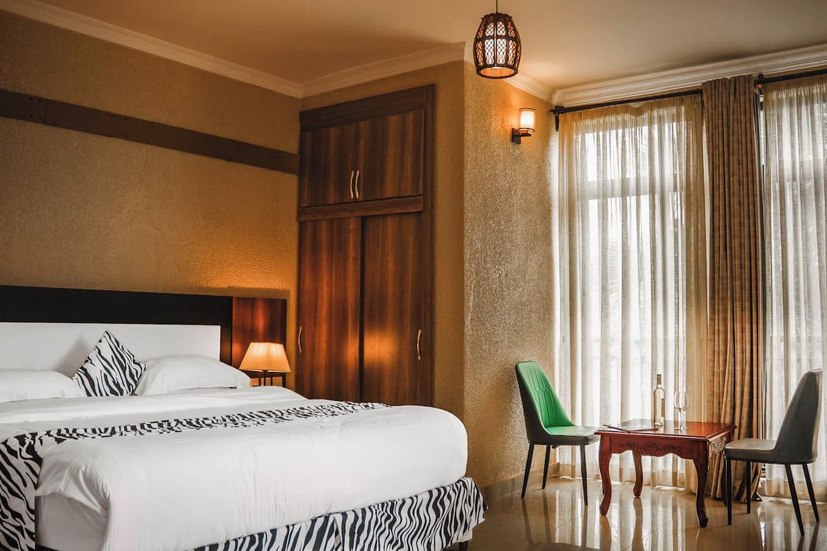 Habitación de hotel con una cama grande, un armario de madera, un escritorio con silla y una ventana con cortinas.