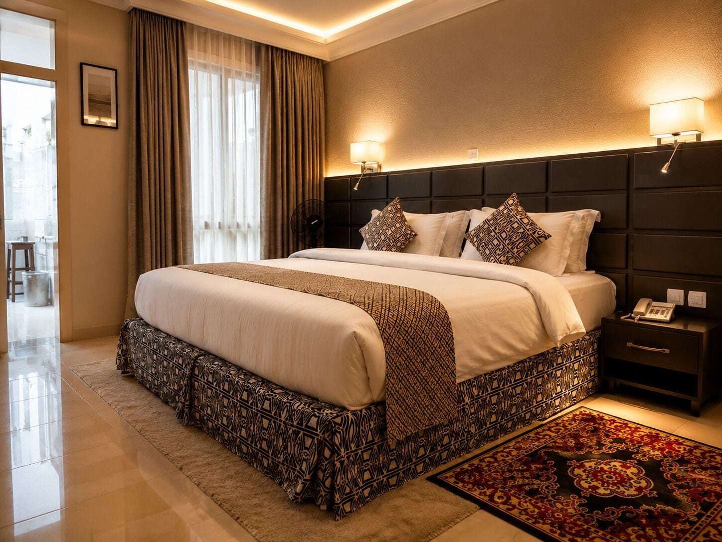A hotel room with a large bed, bedside lamps, a telephone, and a patterned rug.