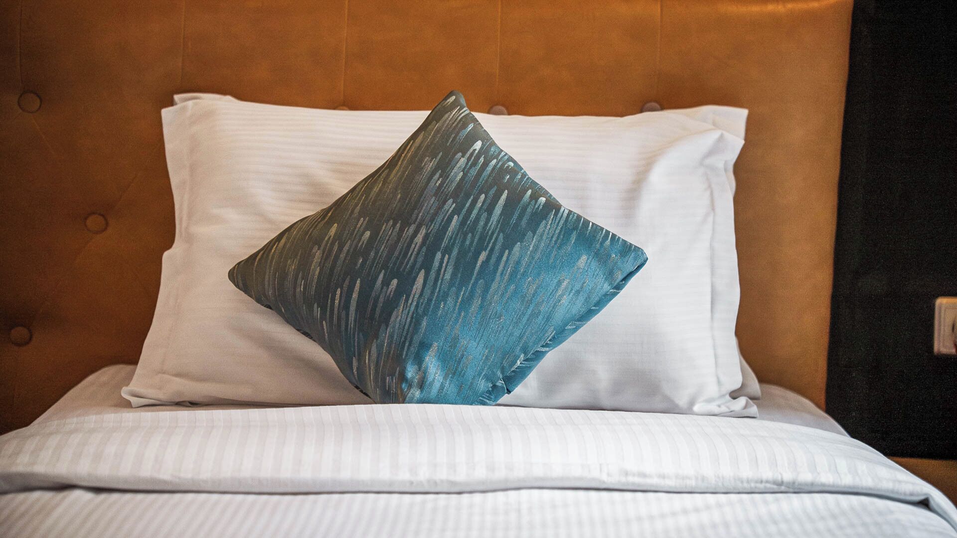 A bed with a white pillow and a blue patterned pillow.