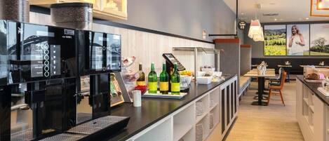 A modern kitchen with a coffee machine, a refrigerator, and a counter with bottles and a coffee pot.