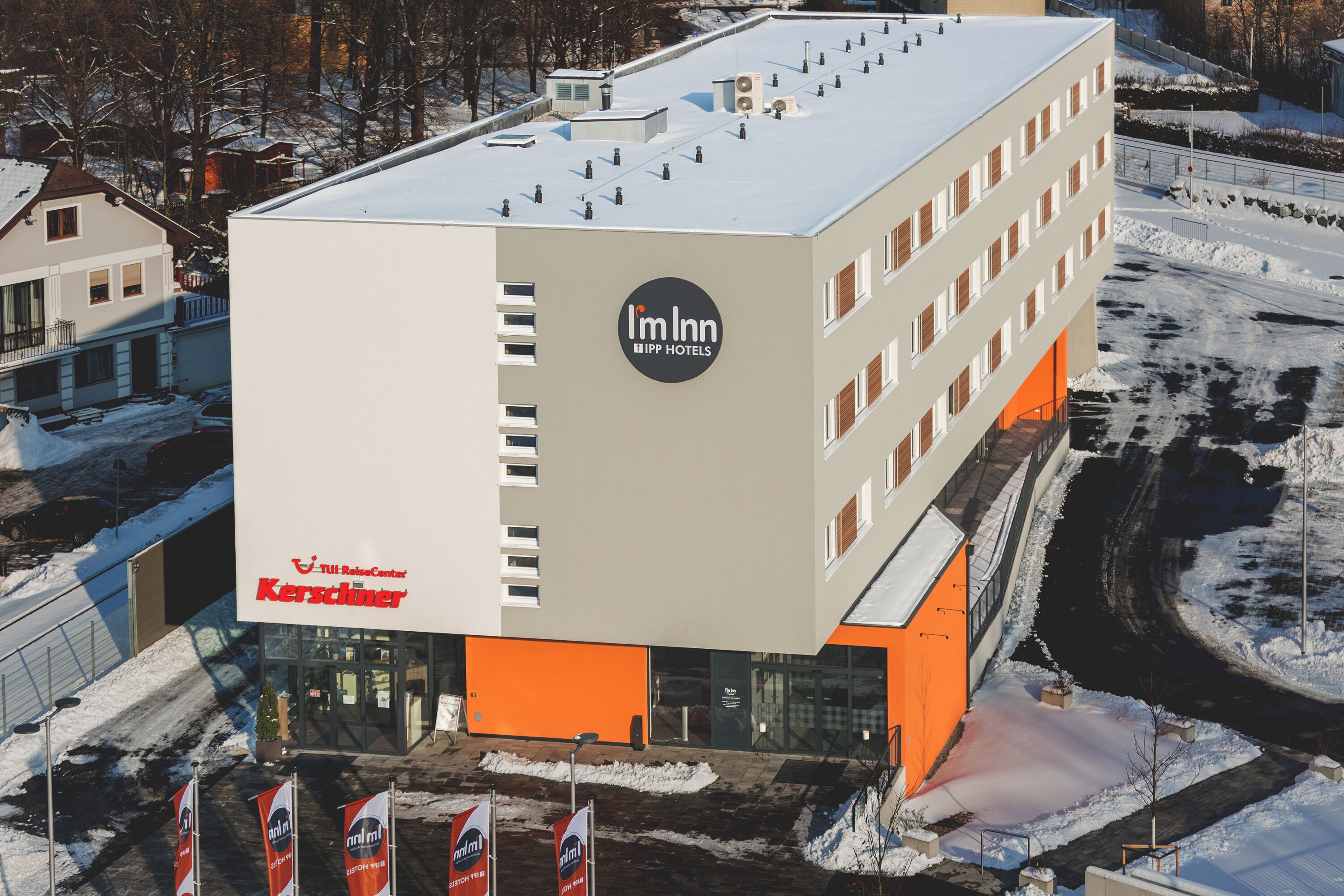 A modern hotel building with a prominent 'Im Inn' sign, featuring a flat roof and multiple windows.