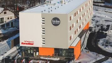 A modern hotel building with a prominent 'Im Inn' sign, featuring a flat roof and multiple windows.