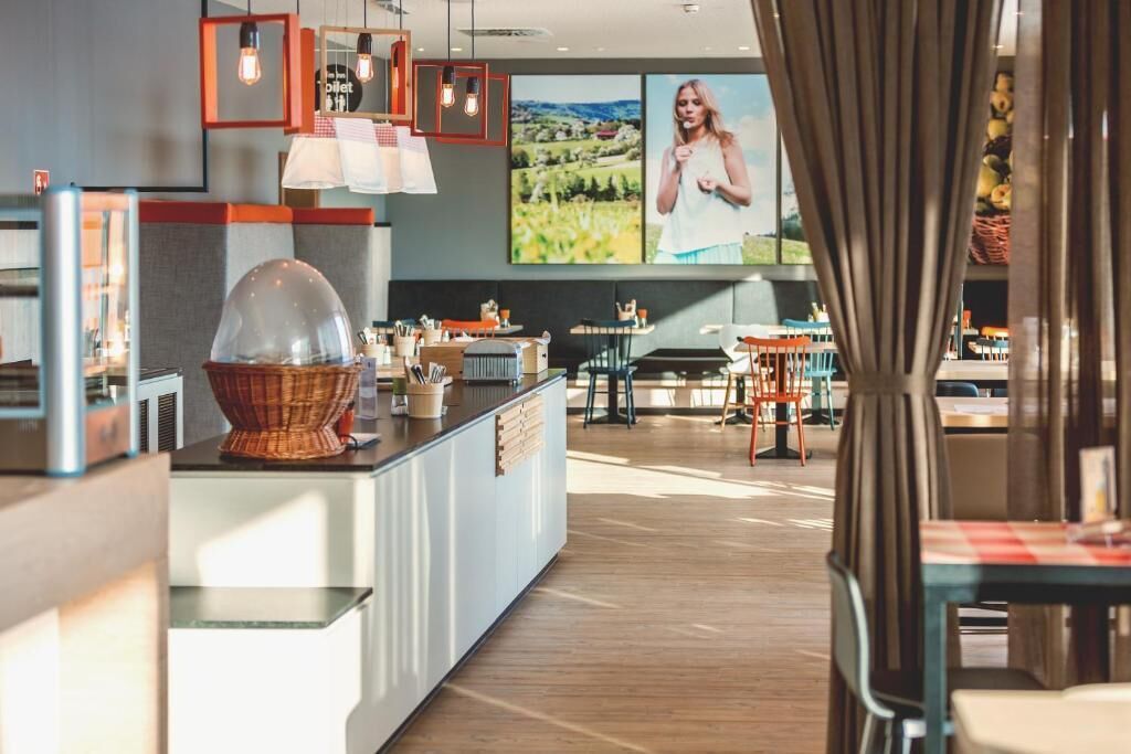 A modern restaurant with a central island, pendant lighting, and a large window with a view of a landscape.