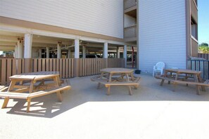 Un espace extérieur aménagé en terrasse, avec des tables et des bancs en bois, une chaise en plastique blanc et une clôture en bois.