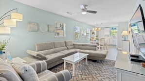 Un salon moderne avec un canapé d’angle, une table basse en verre et un ventilateur de plafond.
