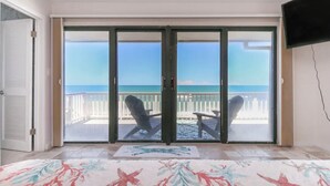A room with a large sliding glass door leading to a balcony with a view of the sea.