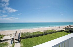 Une vue sur la plage depuis un balcon doté d’une terrasse en bois, d’une pelouse et d’une clôture en bois.