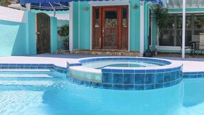 A swimming pool with a blue tiled edge, a wooden door, and a covered patio area.