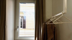 Ein schmaler Flur mit einem Fenster, einem Kleiderständer mit Kleidung und einer kleinen Pflanze.