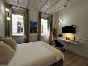 A bedroom with a bed, a TV mounted on the wall, a small desk with a chair, and a window with curtains. - Suites Pantheon Rome - 2  (Roma)