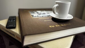 Eine Fernbedienung, eine weiße Tasse auf einem Untertasse und ein Buch mit dem Titel 'The Edet'.